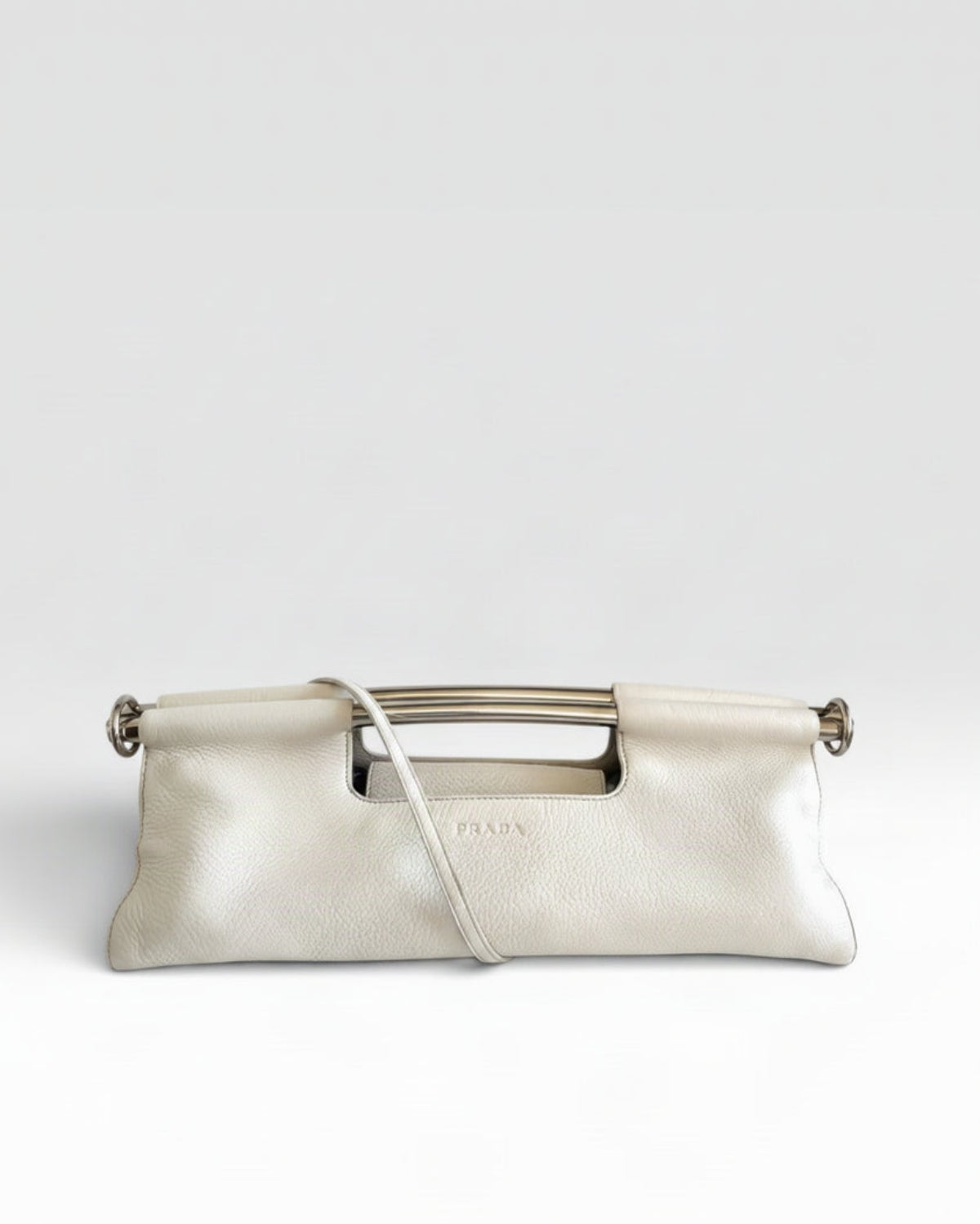 Prada cream-colored pebbled leather clutch bag with a silver-tone metal handle and a matching leather shoulder strap, shown against a light gray background.